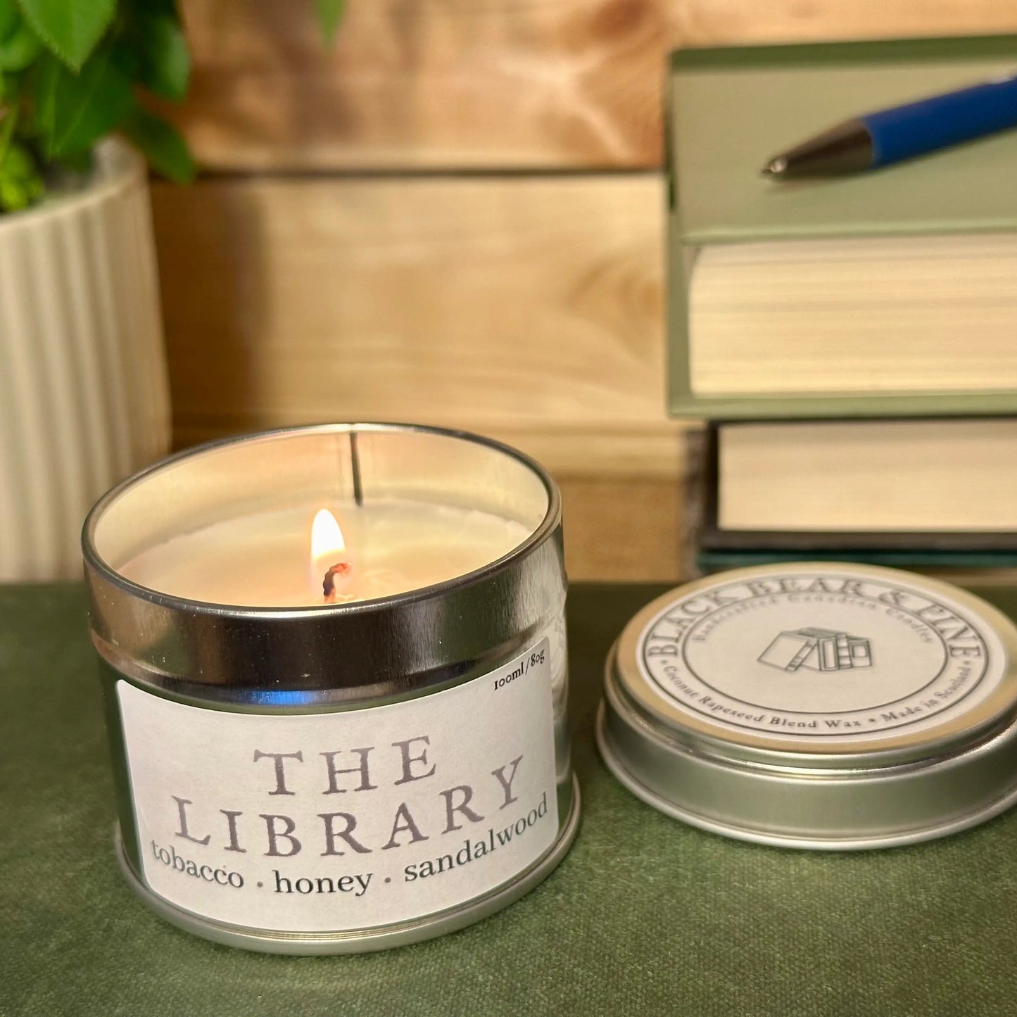Candle labeled 'The Library' with a stack of books and pen in the background
